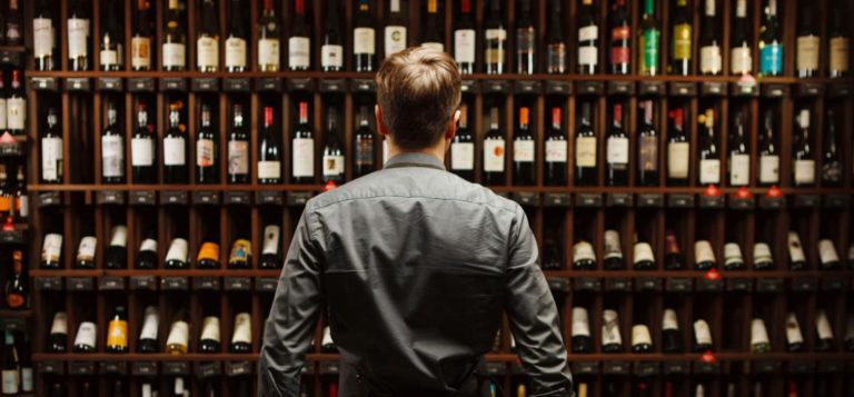 A man stands in front of a rack of wine.
