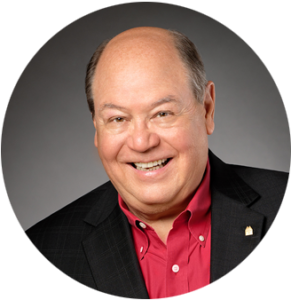 Bob Monica stands smiling while wearing a black jacket and red collared shirt