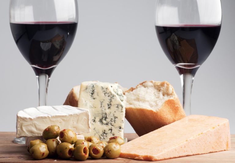 Two glasses of wine with cheese, green olives, and bread between them.