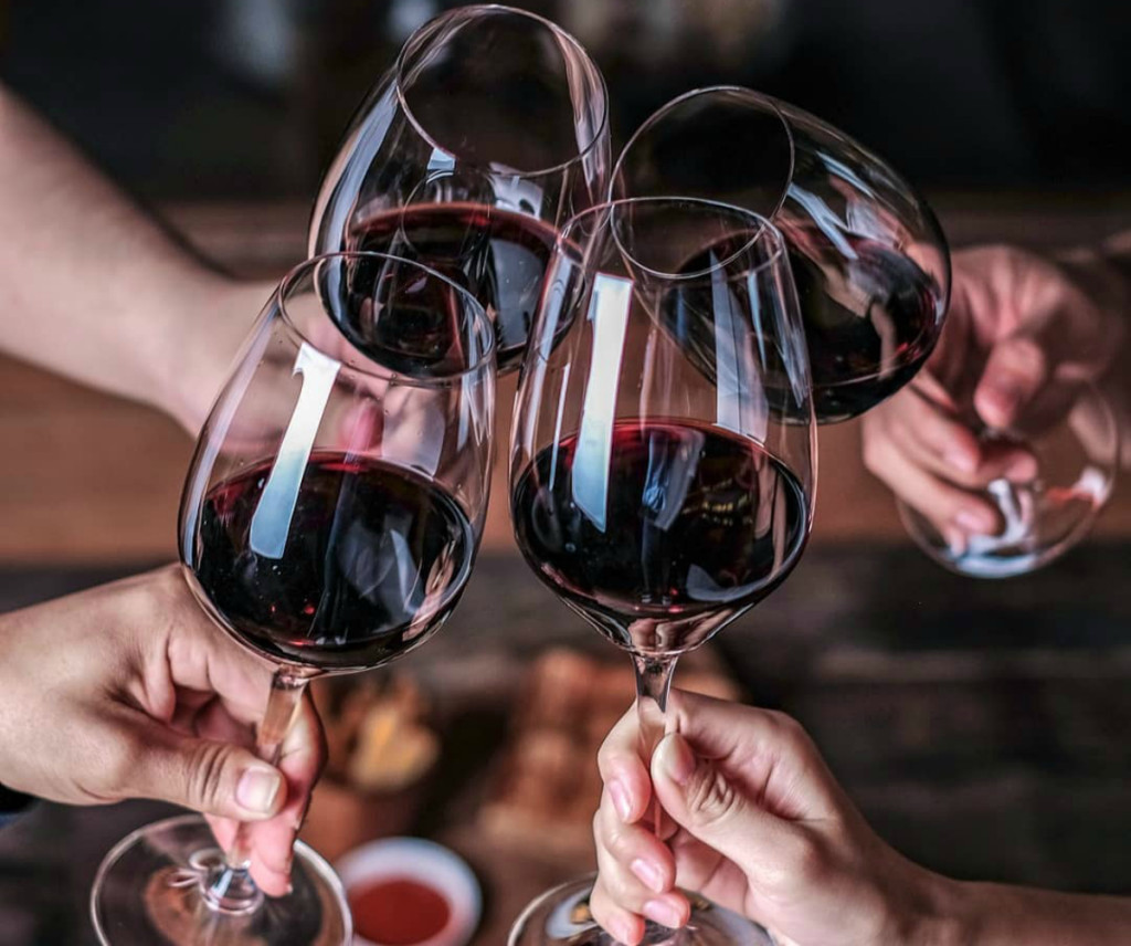 A group of people sit at a table while clinking their wine glasses together